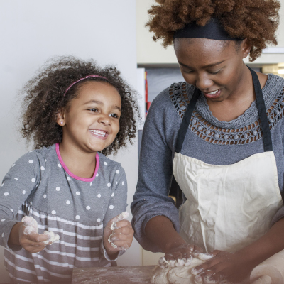 Smiling woman and young girl kneading dough together in a kitchen.