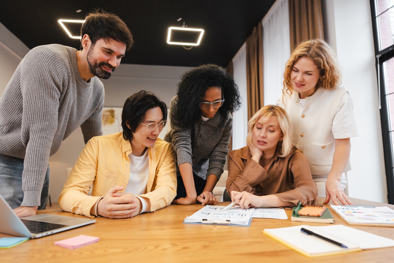 Group of five diverse people collaborating and discussing charts and documents on a table in a modern office.