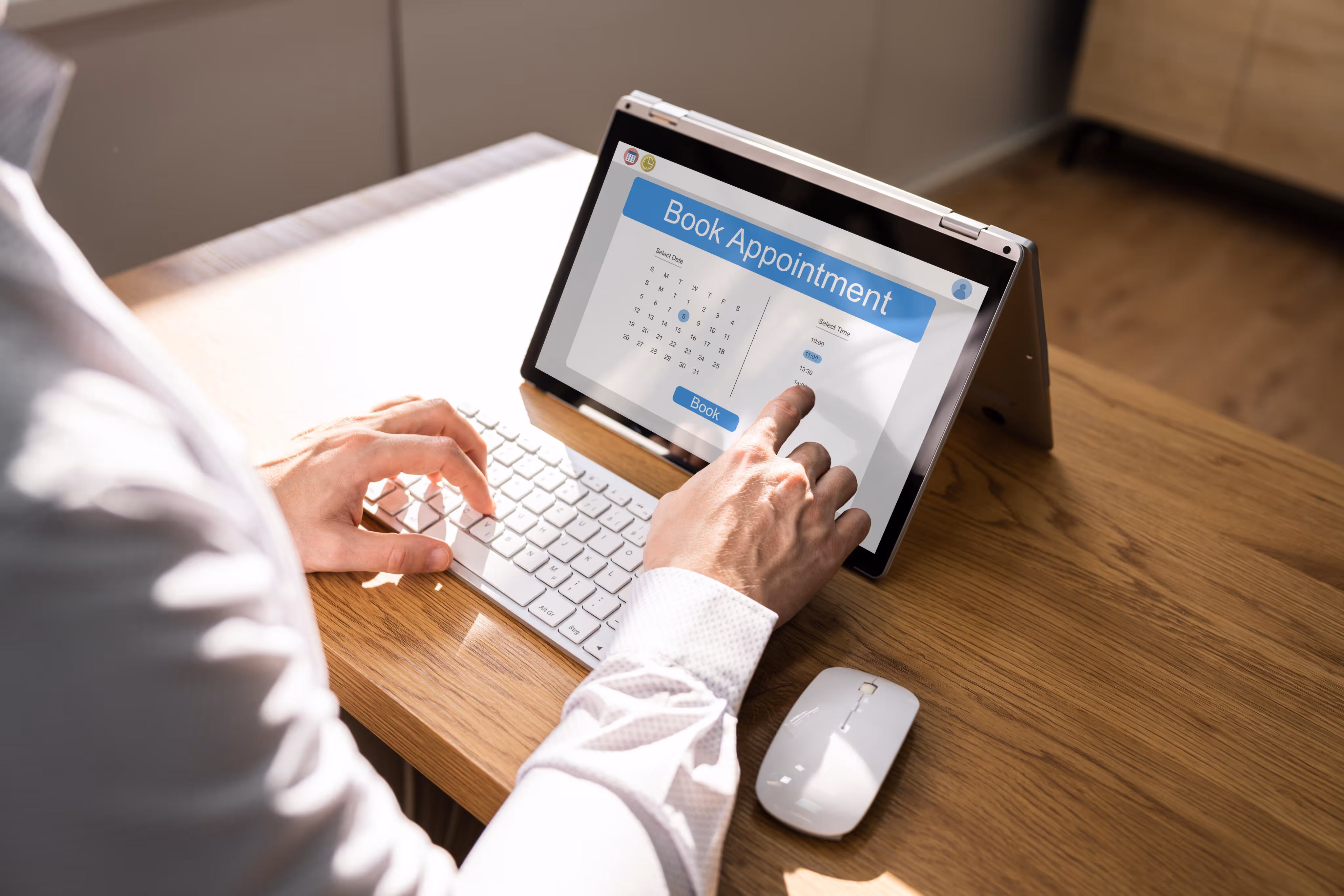 Person booking an appointment on a tablet displaying a calendar and time options while typing on a keyboard.
