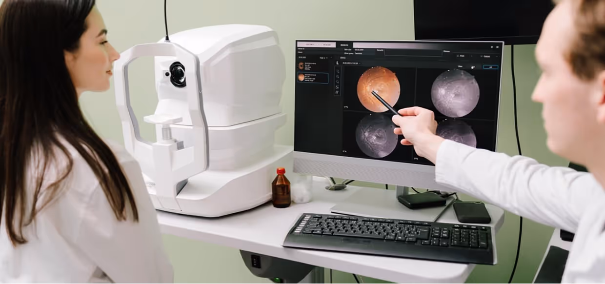 Eye care professional points at retinal images on a computer screen while a patient looks on during an eye examination.