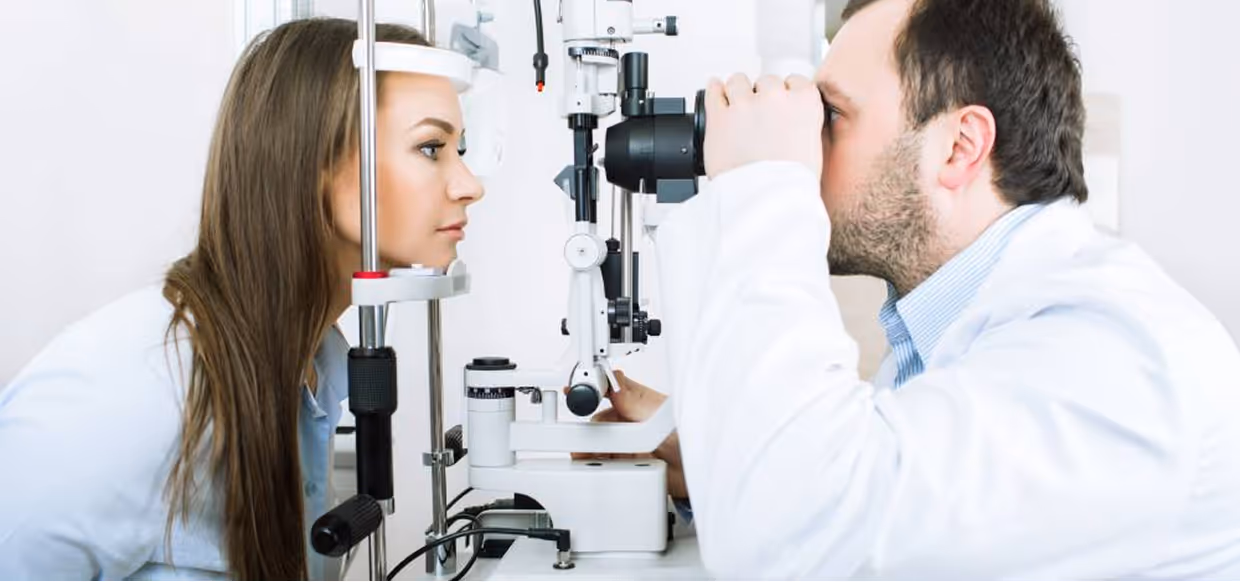 Female patient undergoing an eye examination using a slit lamp by a male optometrist in a clinical setting.