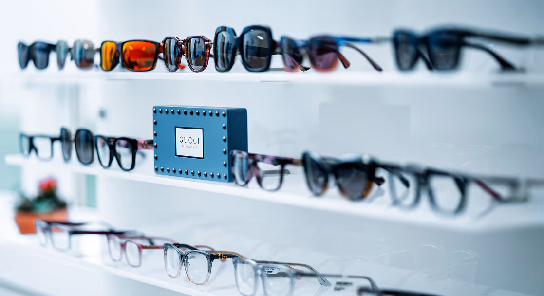 Shelves displaying various styles of eyeglasses and sunglasses, with a blue Gucci official dealer sign in the center.