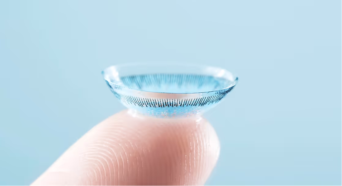 Close-up of a colored contact lens balanced on the tip of a finger against a light blue background.