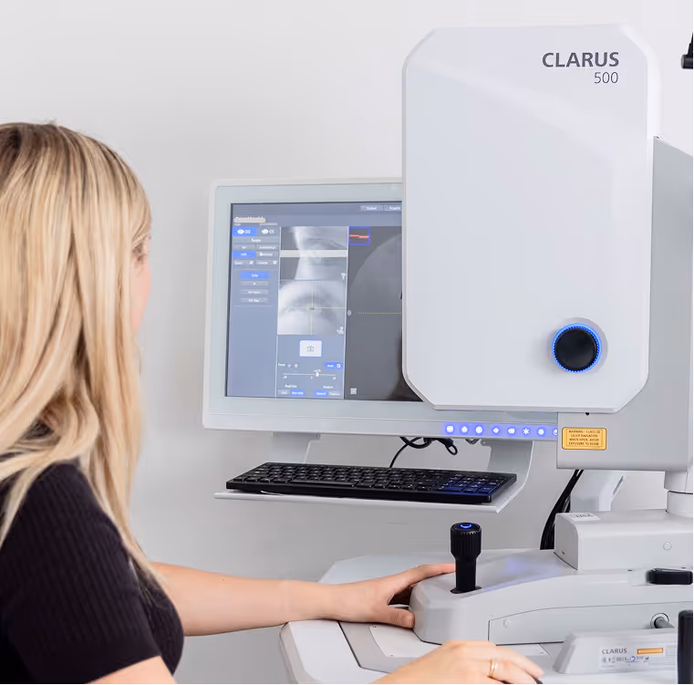 Woman operating a Clarus 500 eye imaging machine with X-ray images displayed on the monitor.