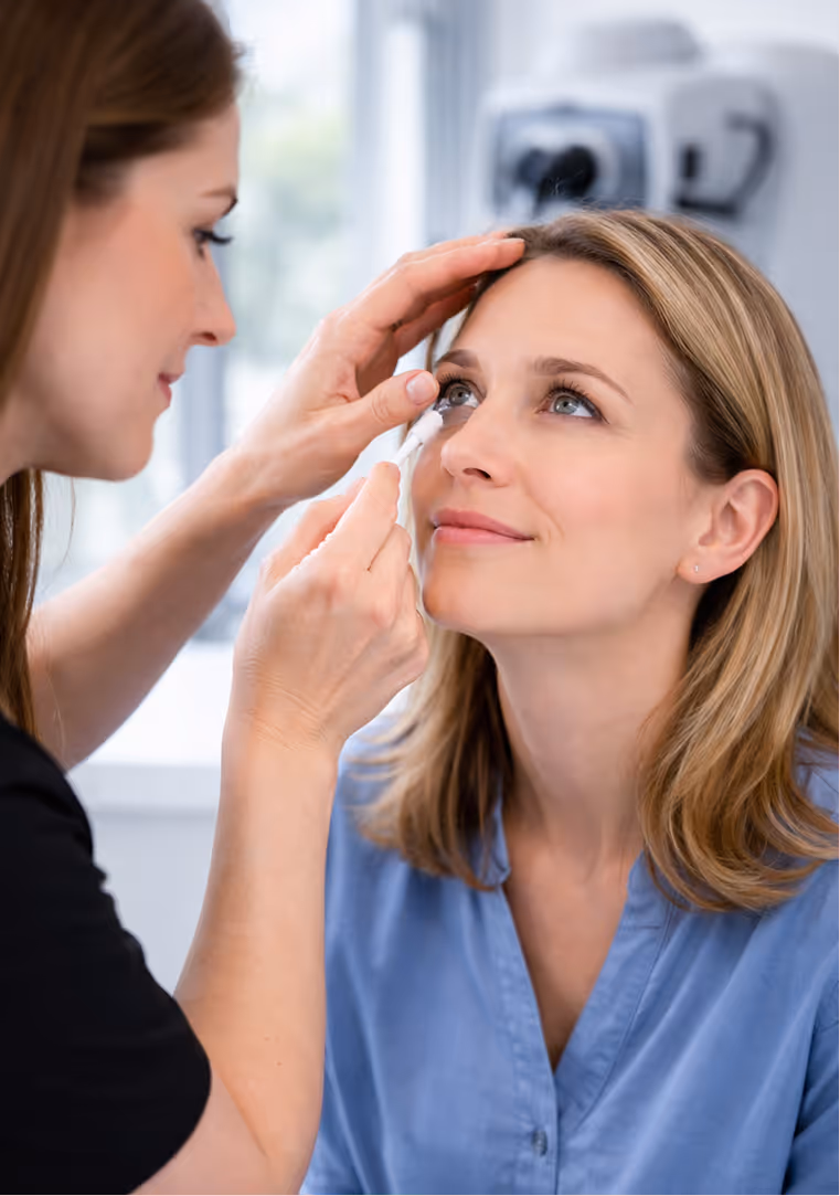Woman in blue shirt receiving an eye exam while another woman uses a cotton swab near her eye.