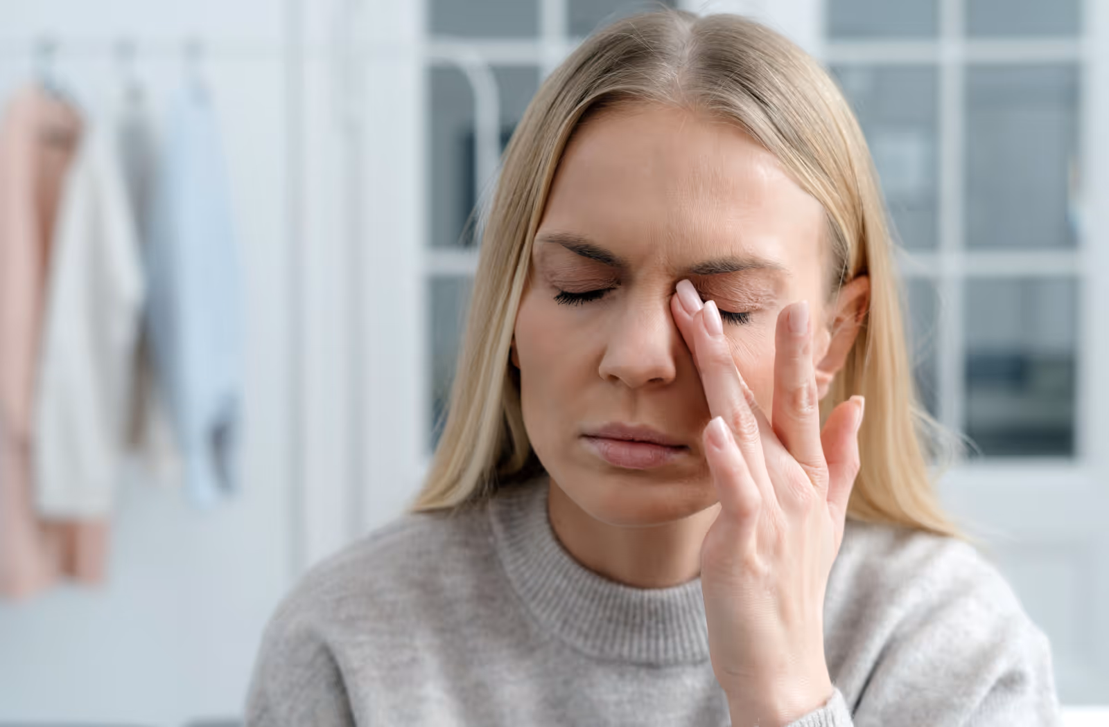 Woman with closed eyes pressing her fingers to the bridge of her nose, appearing stressed or tired.