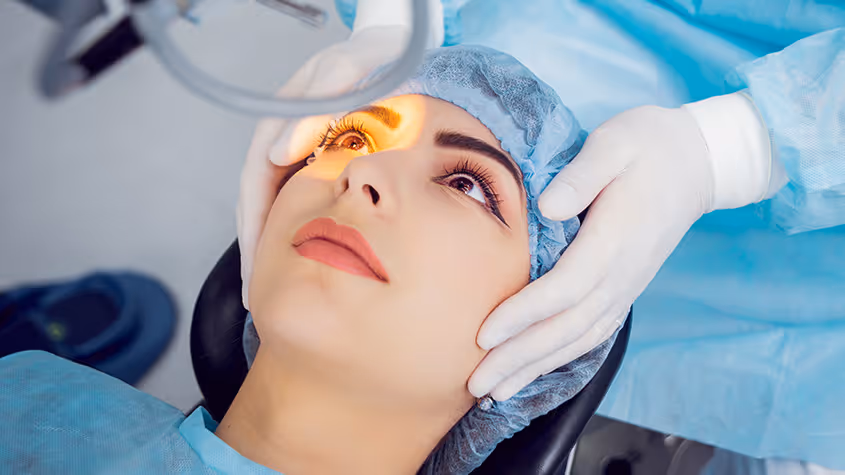 Woman receiving eye examination with light focused on her eye by a healthcare professional wearing gloves and blue gown.