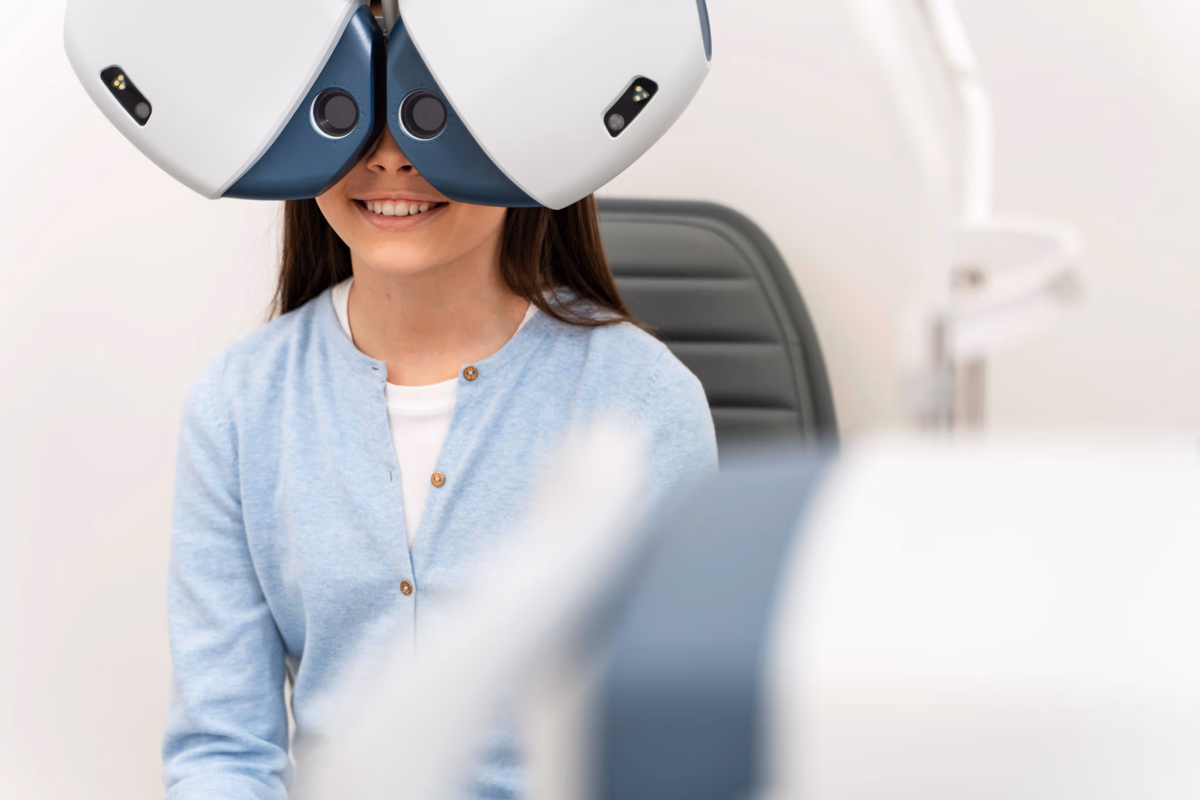 Smiling woman undergoing an eye exam using a phoropter machine in an optometrist's office.