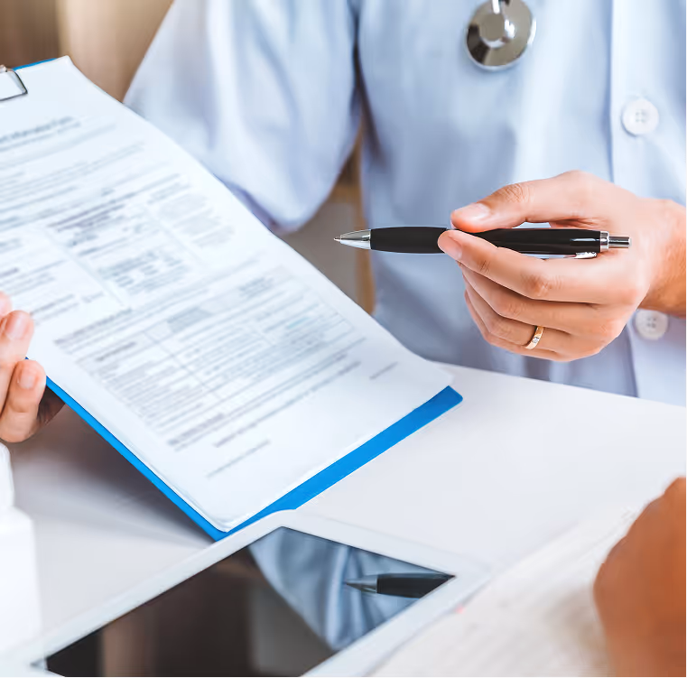 Doctor holding a pen and explaining a medical form on a clipboard to a patient, with a tablet on the table.
