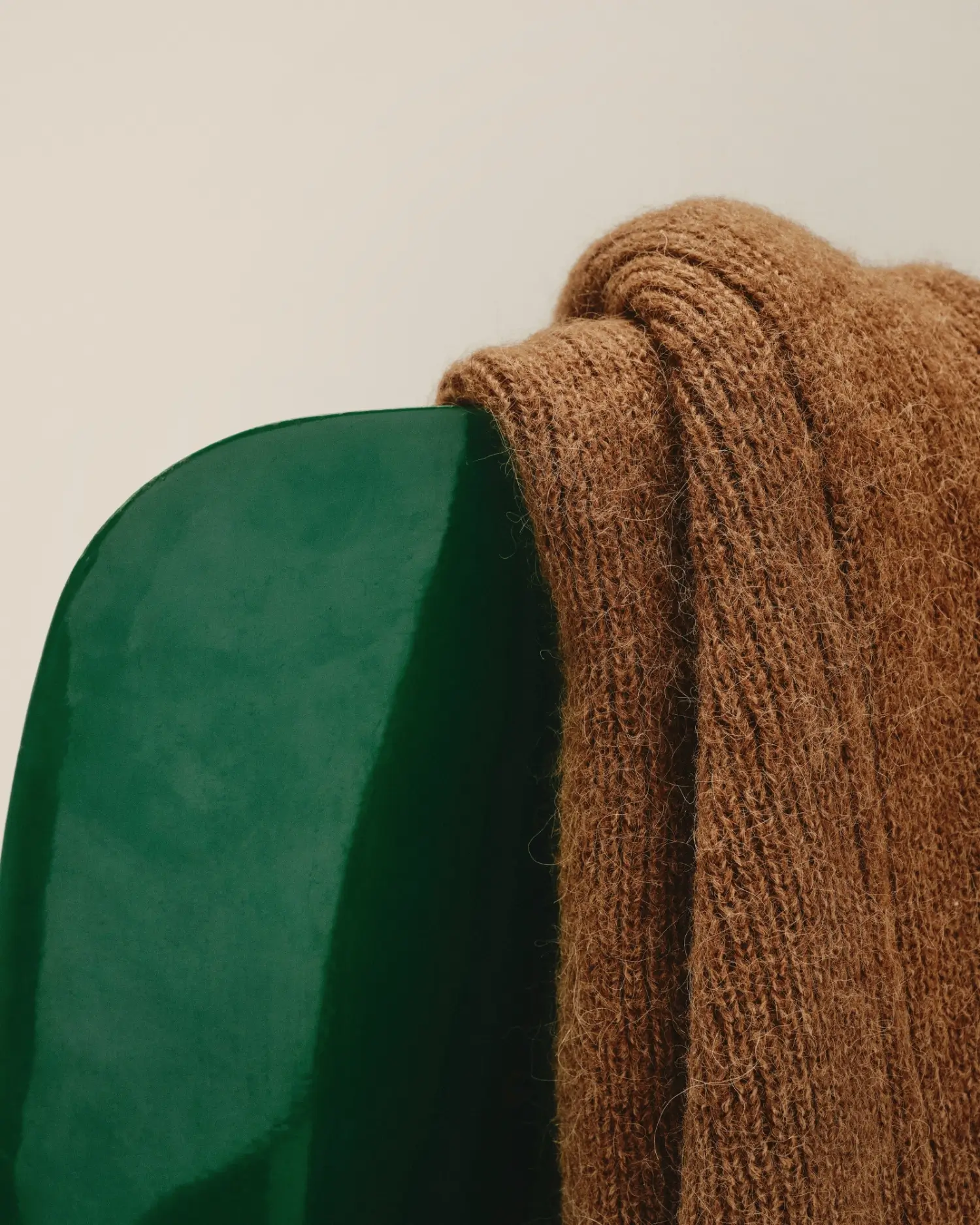 Brown knitted blanket draped over the corner of a dark green chair against a beige wall.