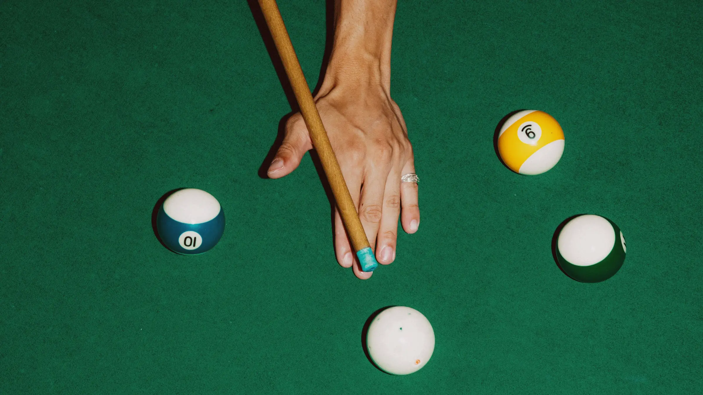 Hand holding a pool cue aiming at billiard balls on a green felt table.
