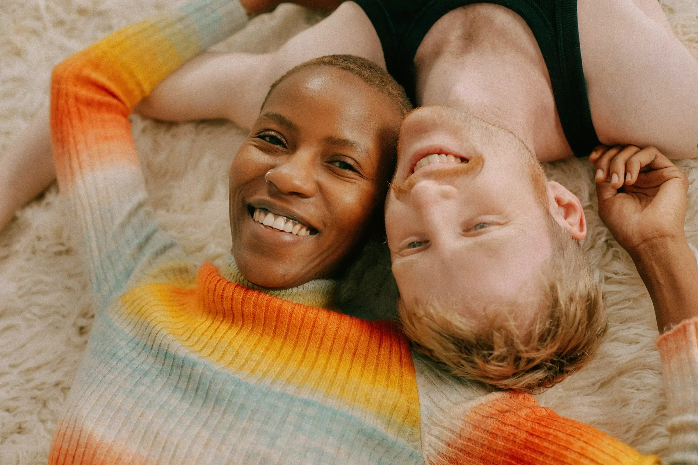 Smiling couple lying on a fluffy rug with heads close together.
