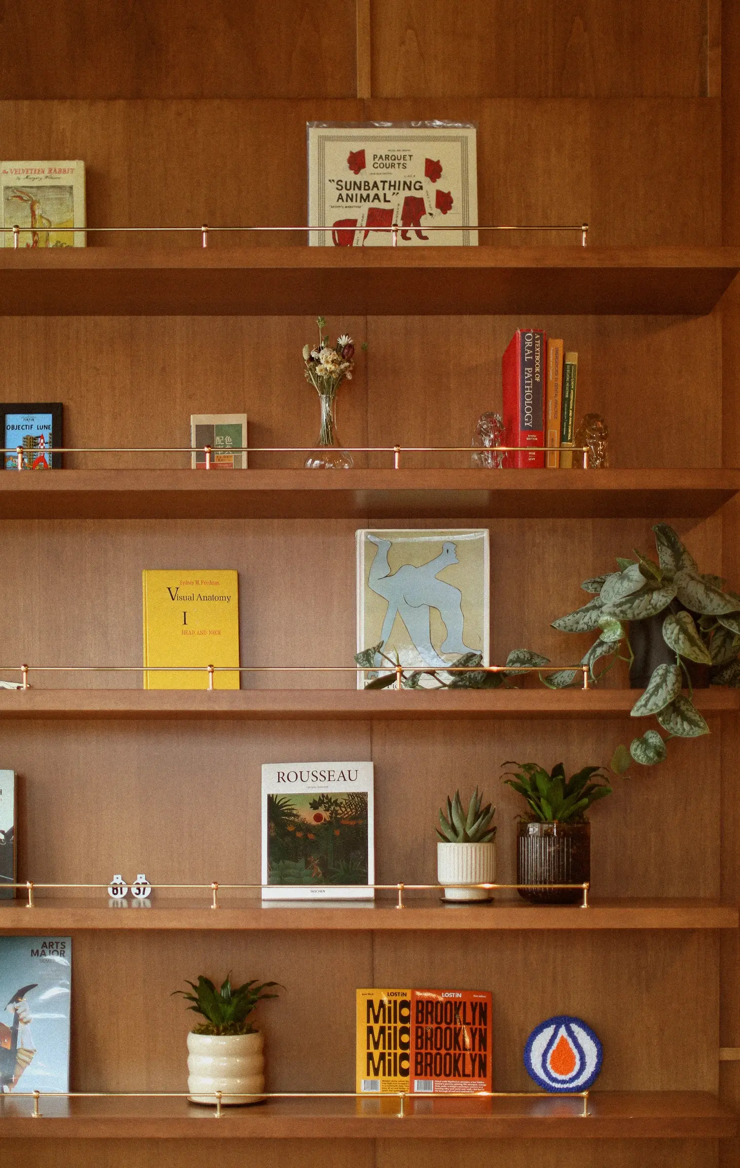 Wooden bookshelf with a mix of books, dried flowers, two potted plants, and decorative objects on five shelves.