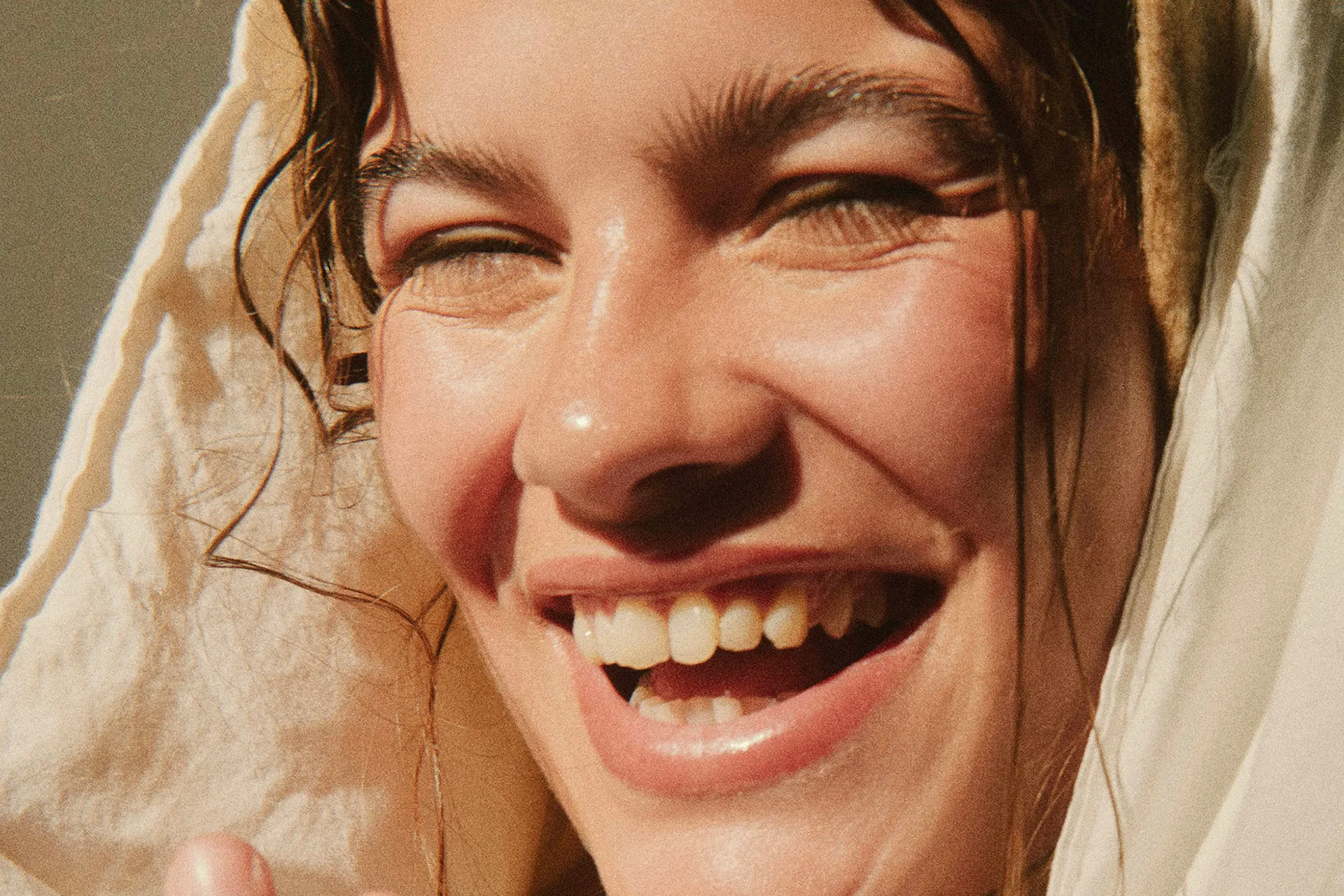 Close-up of a smiling person with eyes closed and hair partially covered by a light fabric.