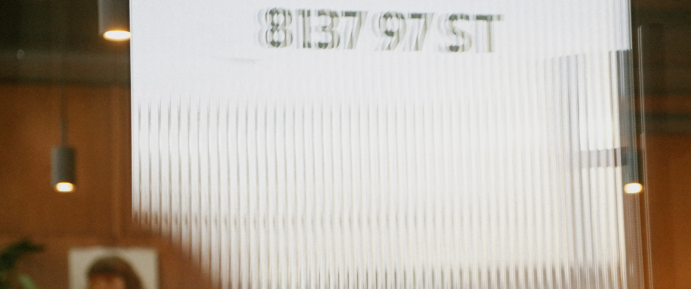 Blurred reflection of the address number 8137 97 ST on a ribbed glass surface indoors.
