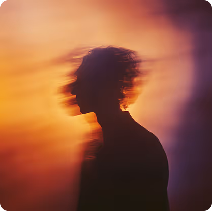 Silhouette of a person with a blurred effect against a warm, gradient background of orange and purple hues.