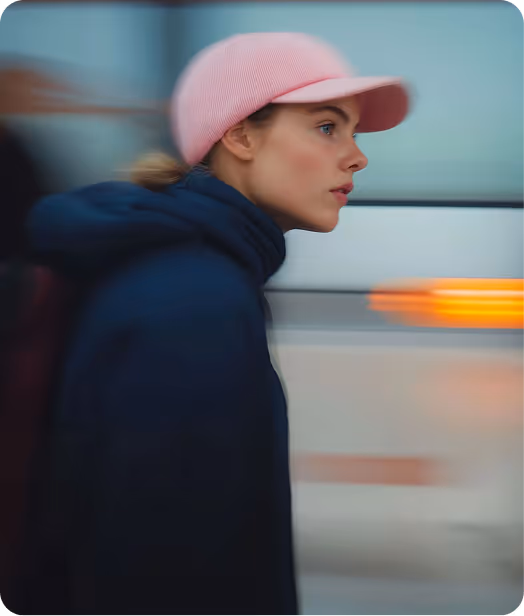 Profile of a young woman wearing a pink cap and dark jacket walking quickly with a blurred background.