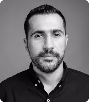 Black and white portrait of a man with short dark hair, a beard, and a black button-up shirt.