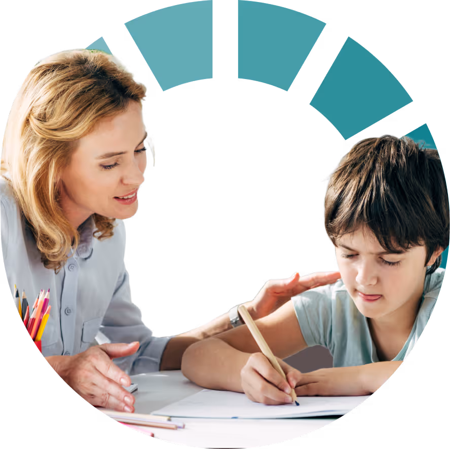 An educational professional gently guides a boy writing at a desk during a social behavioral assessment.