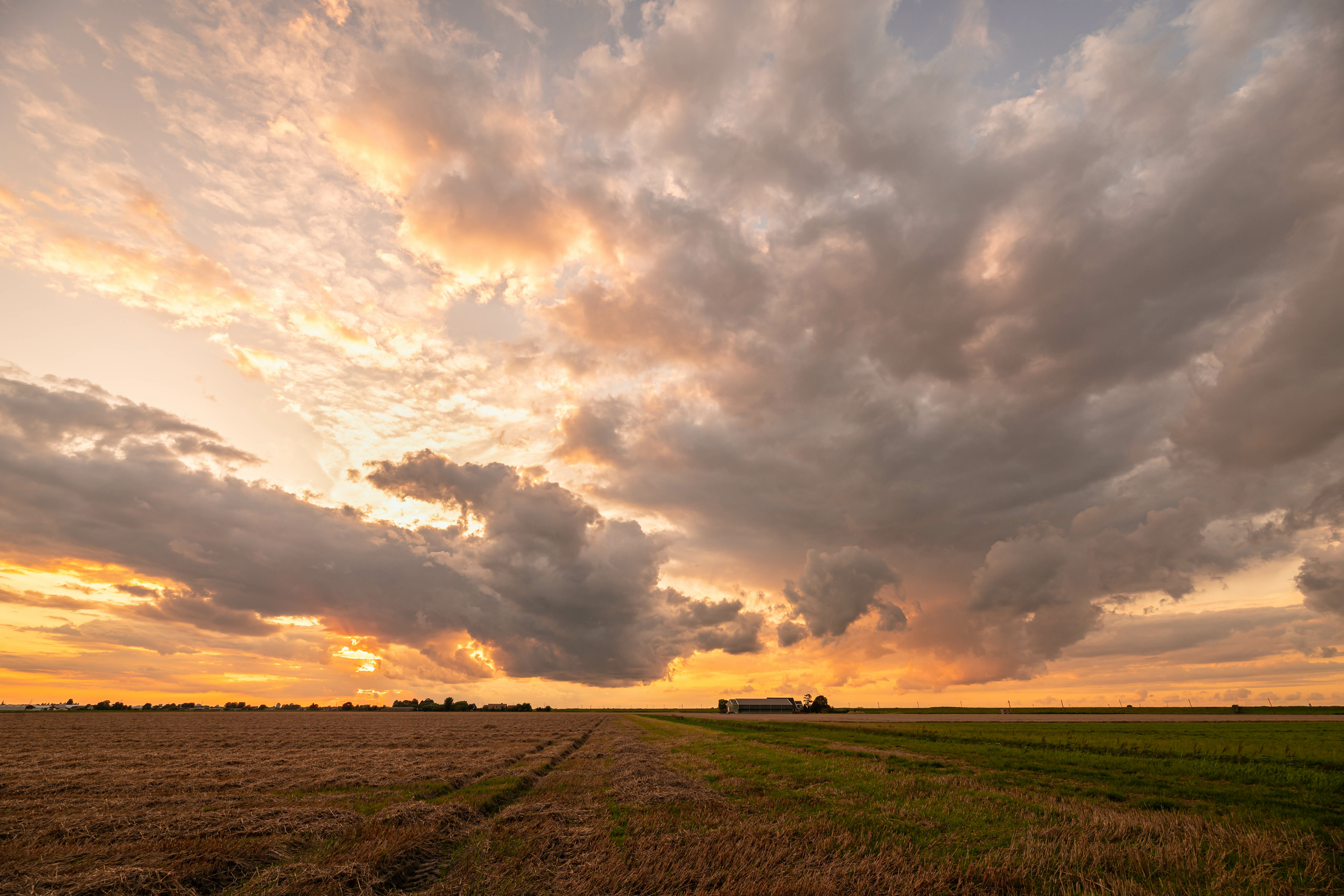 Sunset over open farmland near Yukon, Oklahoma, with dramatic clouds above a harvested field