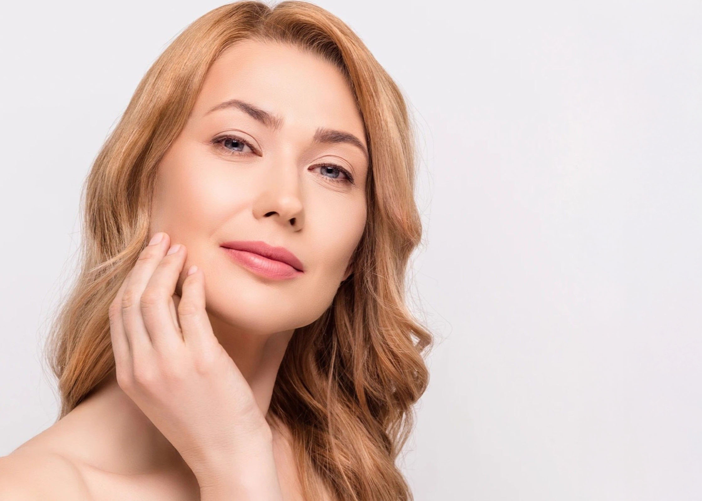 A woman smiling, touching her face