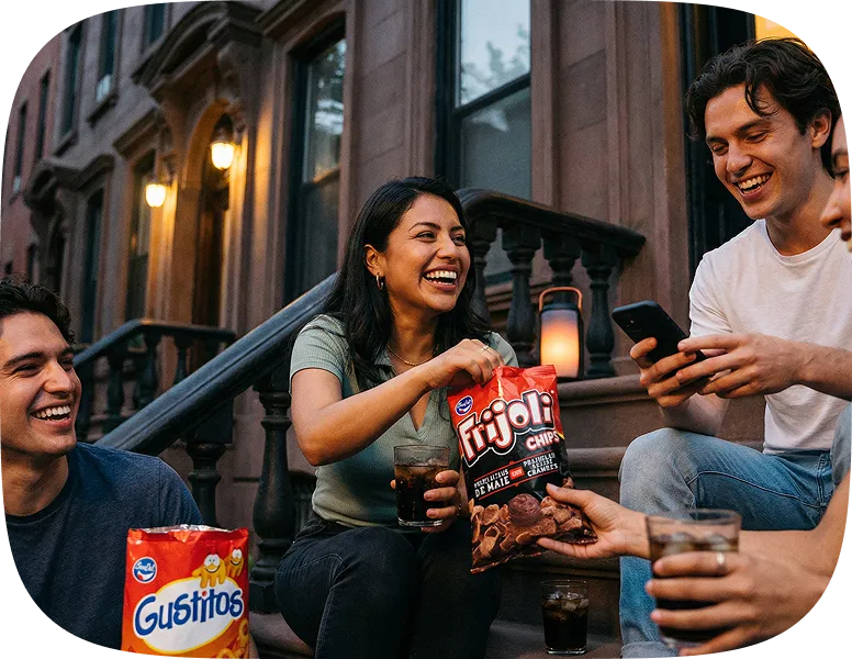 Group of four friends sitting on outdoor steps, smiling and sharing snacks including Frijoli chips and Gustitos, with drinks in their hands.