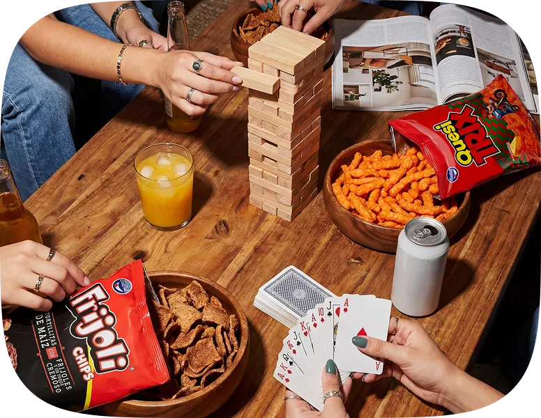 People playing Jenga and cards at a wooden table with snacks, drinks, and an open magazine.