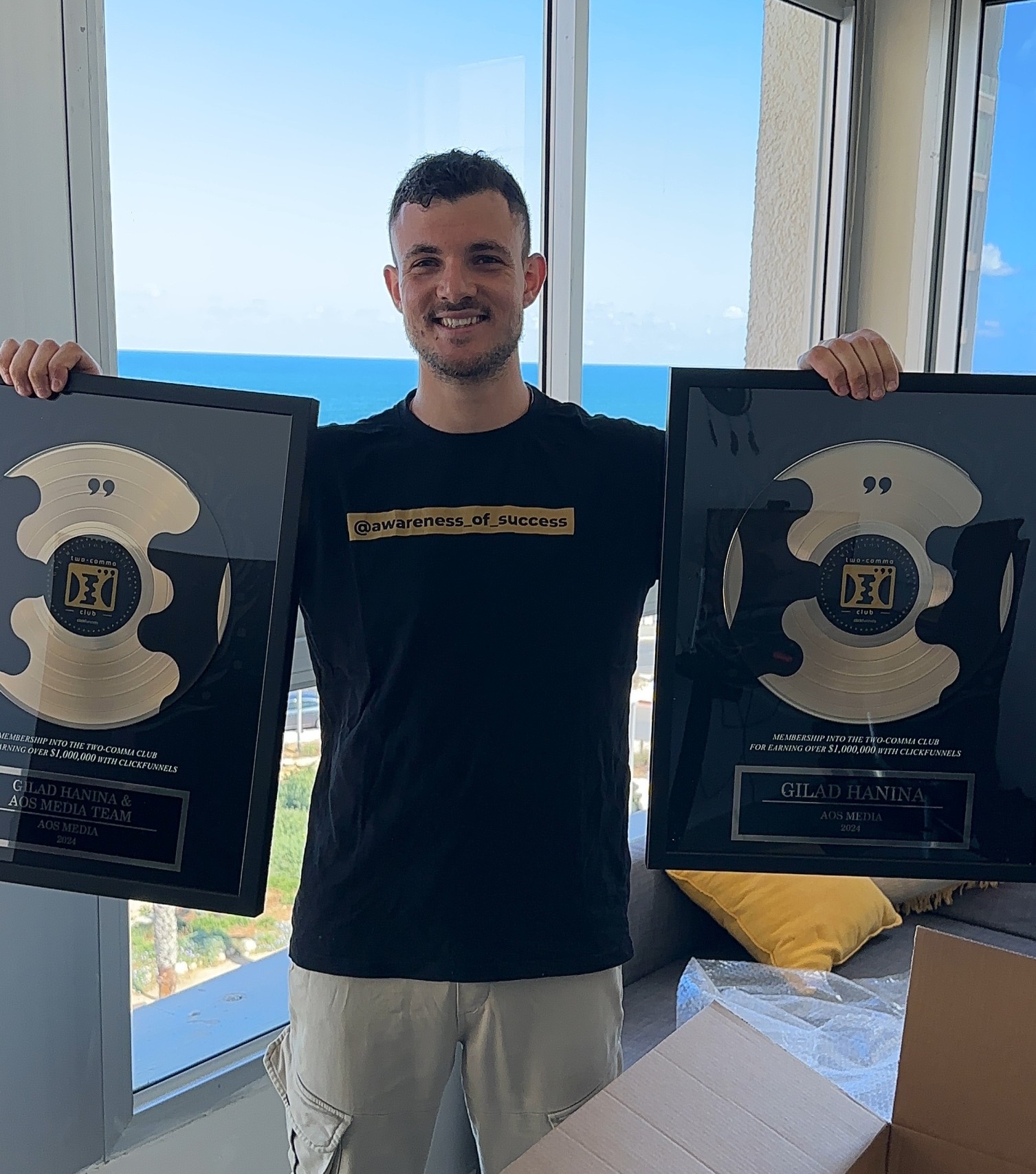 Smiling young person with shoulder-length brown hair wearing a white shirt and dark blazer against a solid dark blue background.