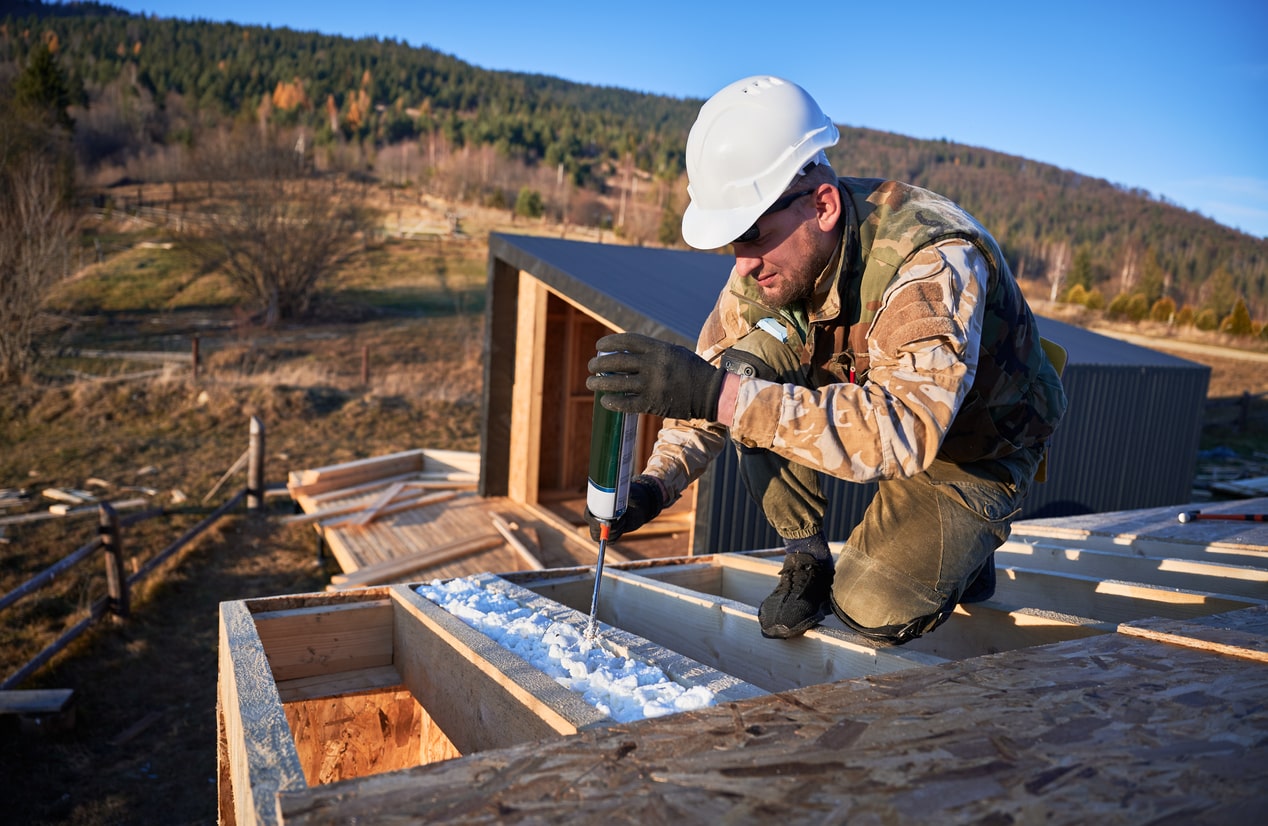 A worker sprays asbestos-containing insulation into the roof of a home under construction.