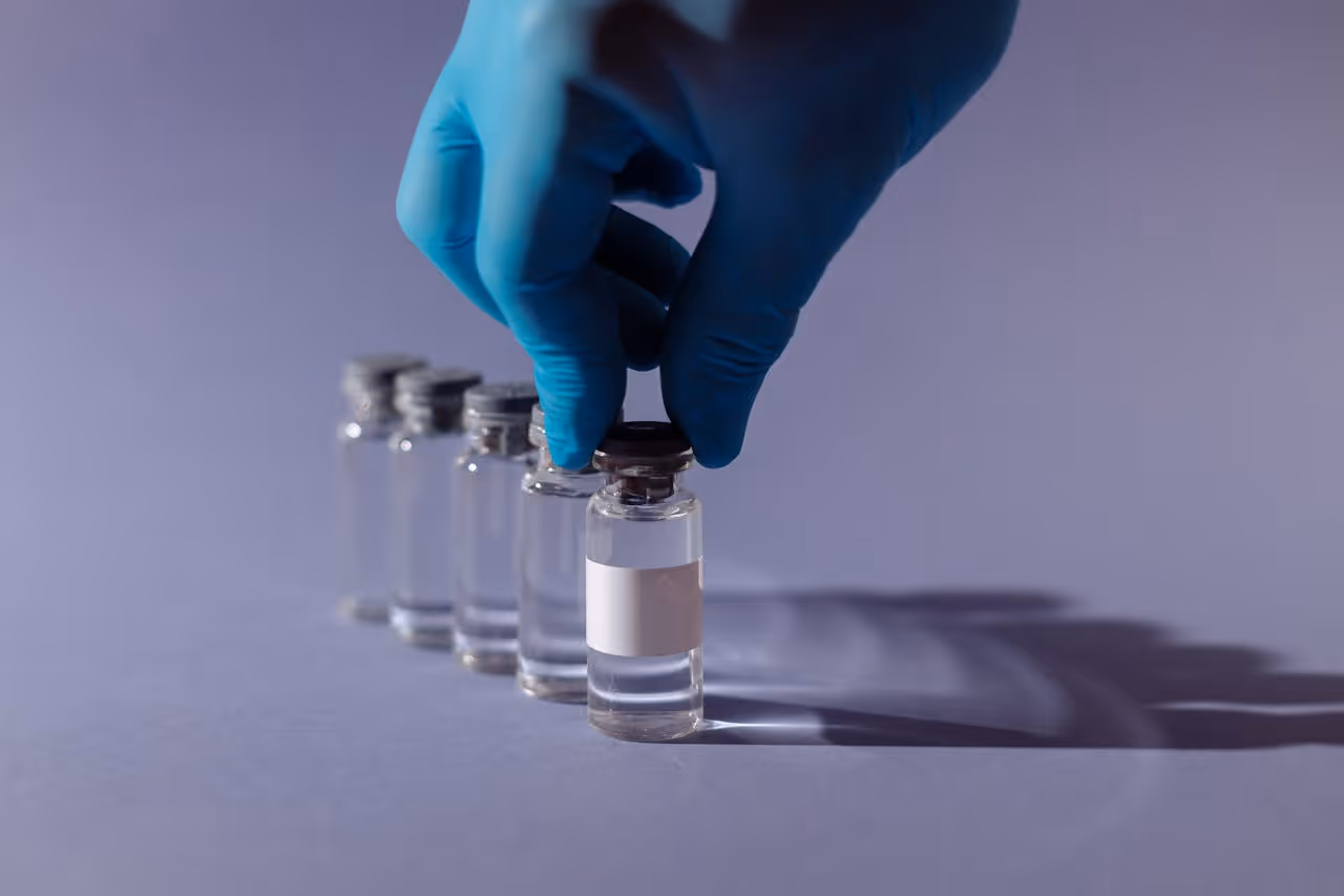 A gloved hand sets down a vial of GLP-1 solution