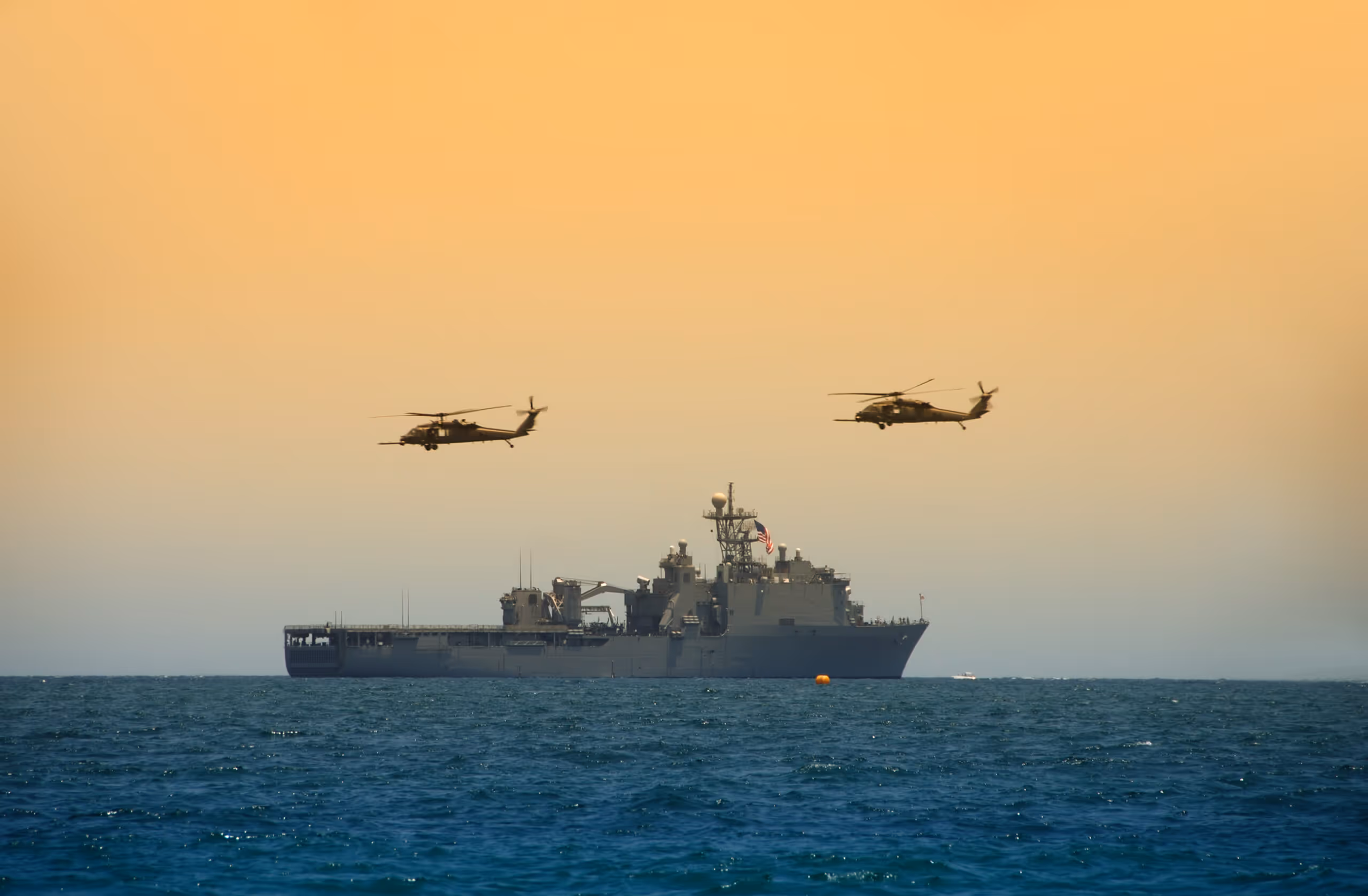 two helicopters hover over a naval war ship