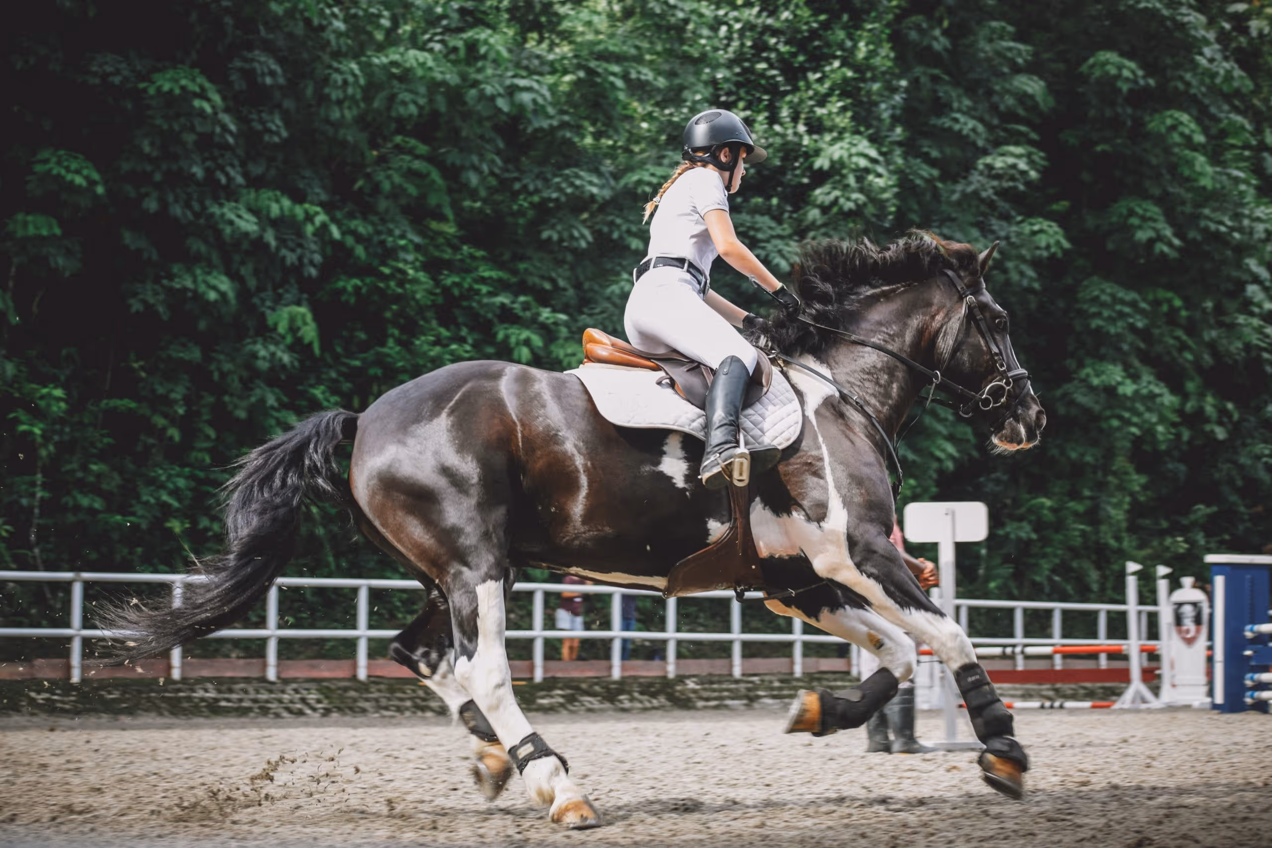 A woman in riding boots and a helmet riding a horse in an enclosure
