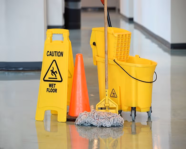 A bucket and mop next to a slippery when wet sign