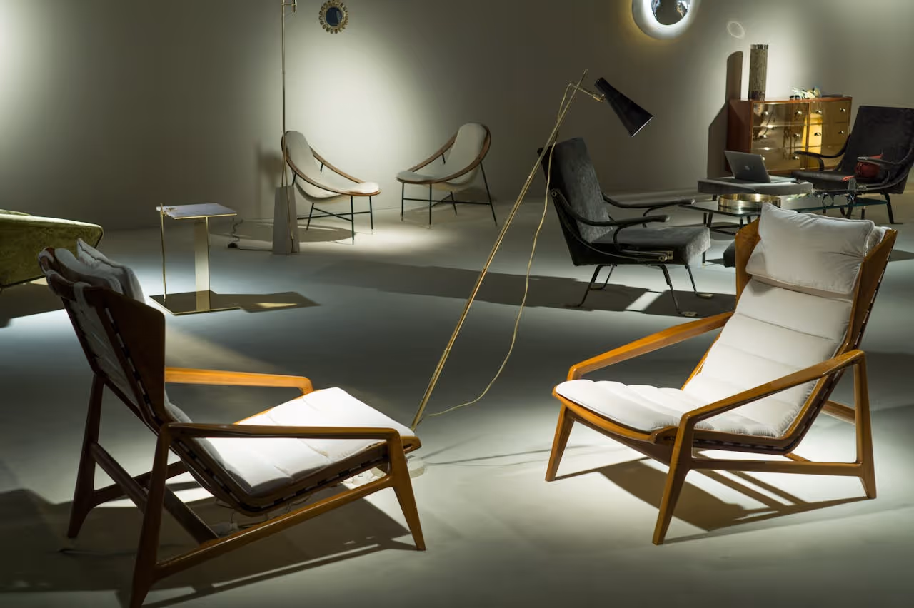 A stylish interior featuring two wooden lounge chairs with white cushions, a floor lamp, and various other modern furniture pieces.