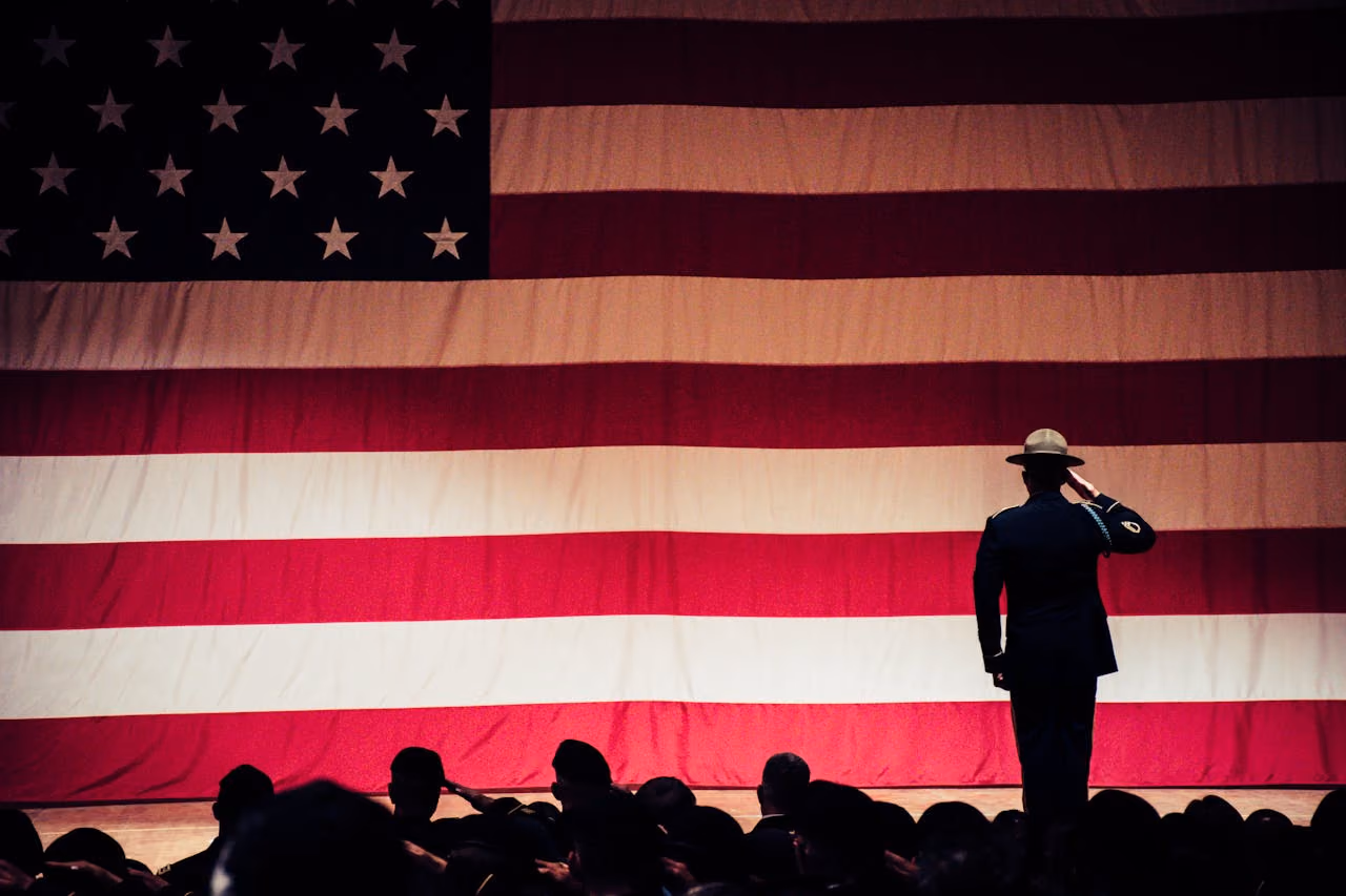 Soldiers in an assembly hall saluting a large american flag on stage