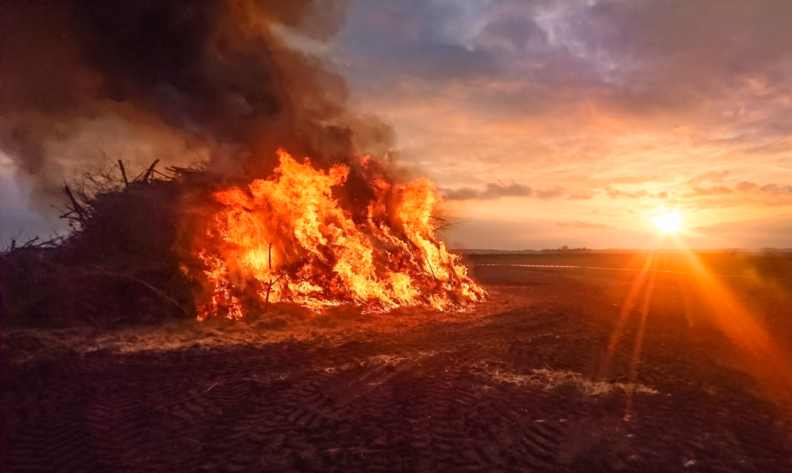 A large burn pit burning  and emitting smoke on open land