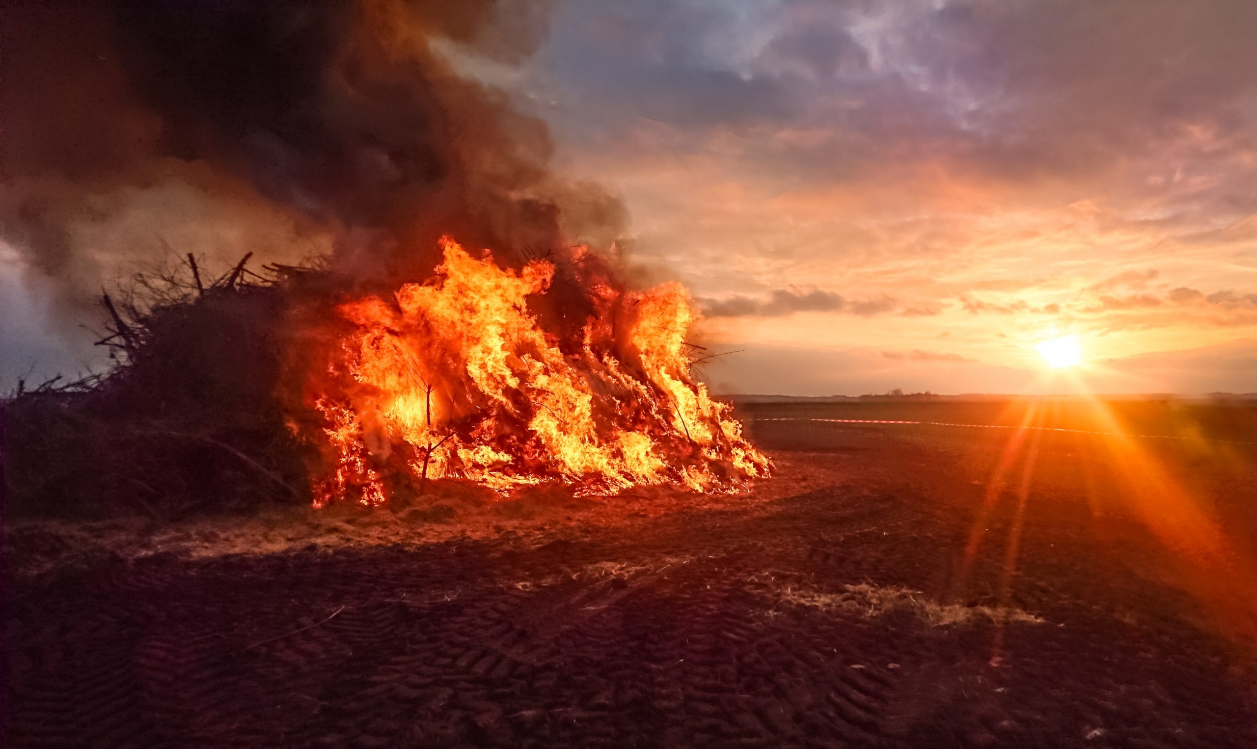 A large burn pit burning and emitting smoke on open land