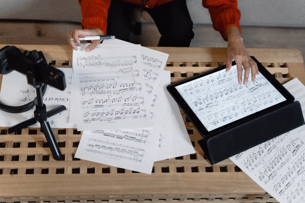 A musician composing on a tablet and writing a score on sheet music