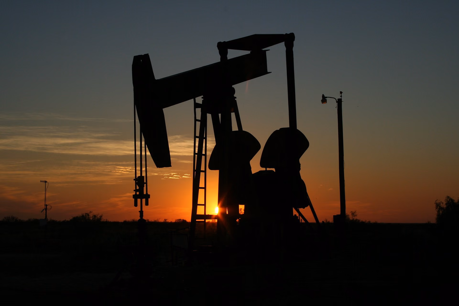 An oil derrick and other fracking equipment seen at sunset