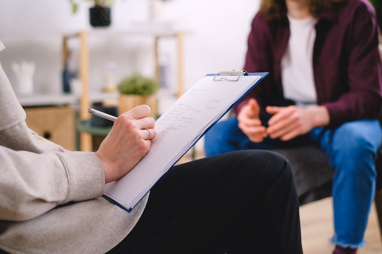 a therapist takes notes whilst talking with a patient