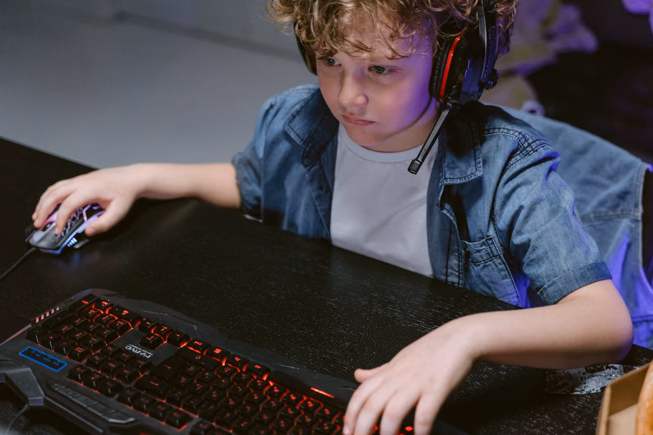 Young boy with headset and gaming console playing on his computer