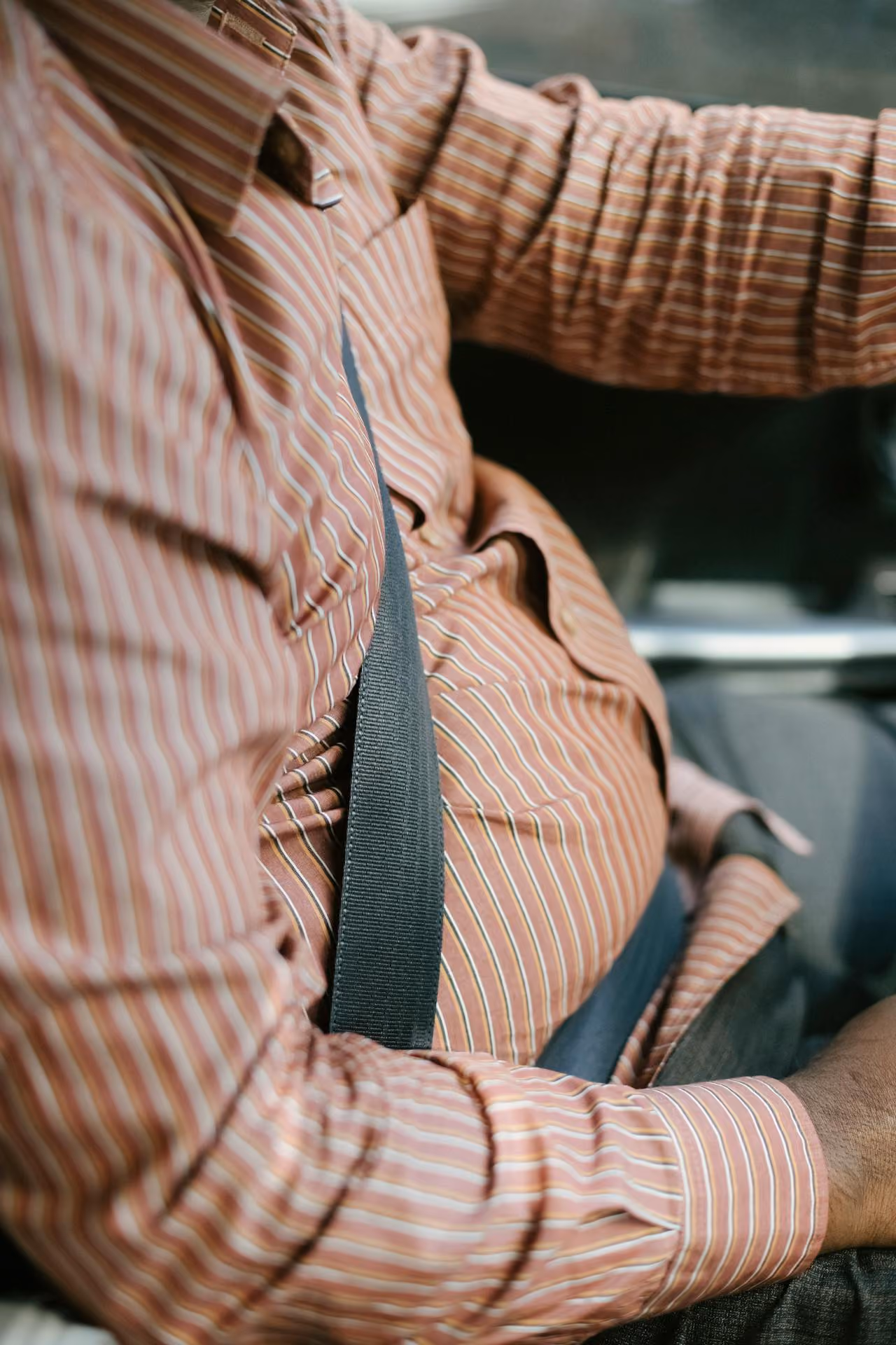 A man in a red striped shirt wears a fastened seatbelt on the driver's seat.