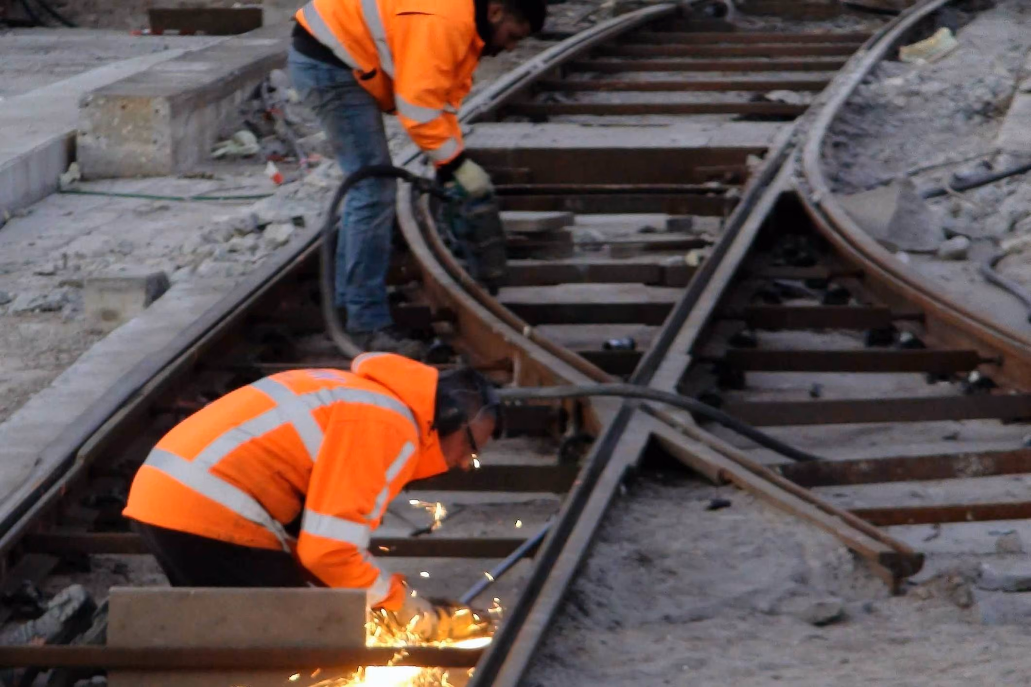 Welders cutting metal on railroad tracks where asbestos exposure may contribute to mesothelioma.