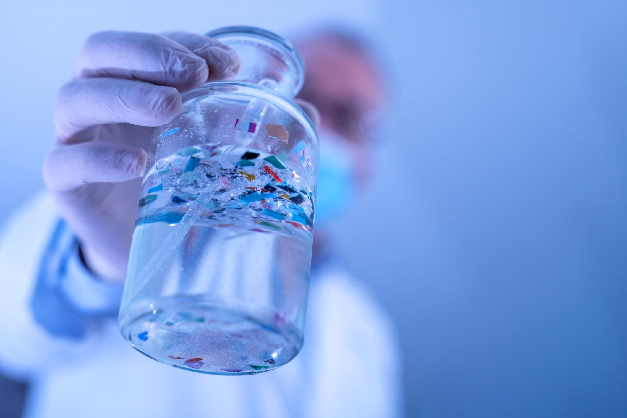 Scientist in protective gear holding a bottle of microplastic particles for a microplastics lawsuit.