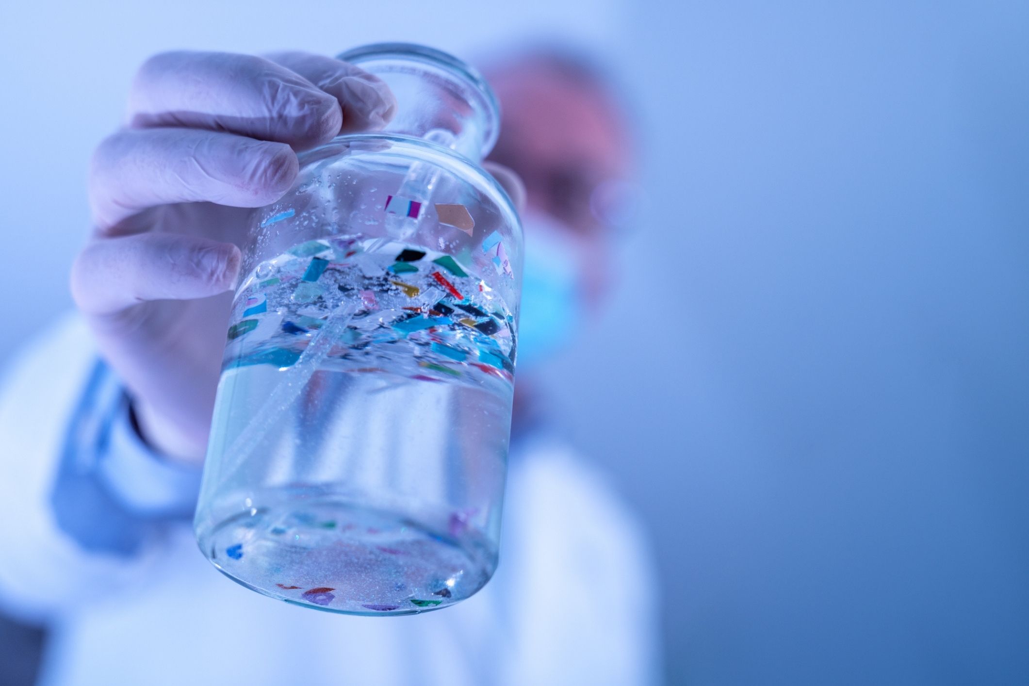 Scientist in protective gear holding a bottle of microplastic particles for a microplastics lawsuit.