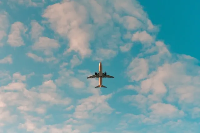 Flugzeug von unten vor blauem Himmel mit weißen Wolken.