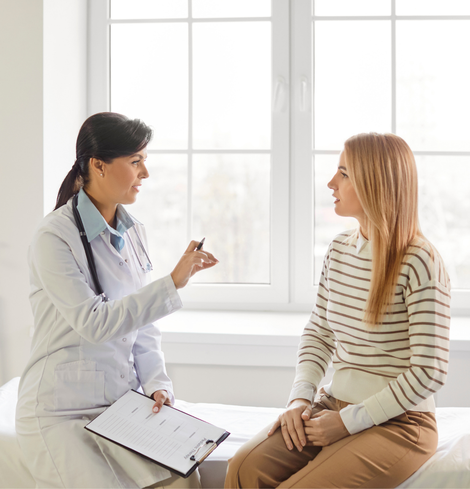Female doctor with a clipboard consulting a female patient in a bright medical office.