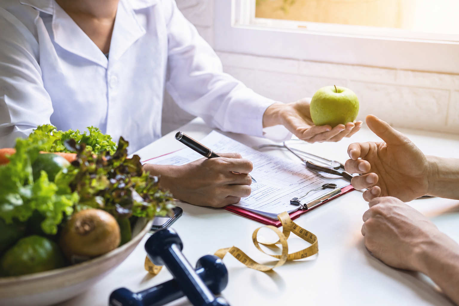 Person in white coat offers green apple while writing on clipboard, with healthy food and weights nearby.