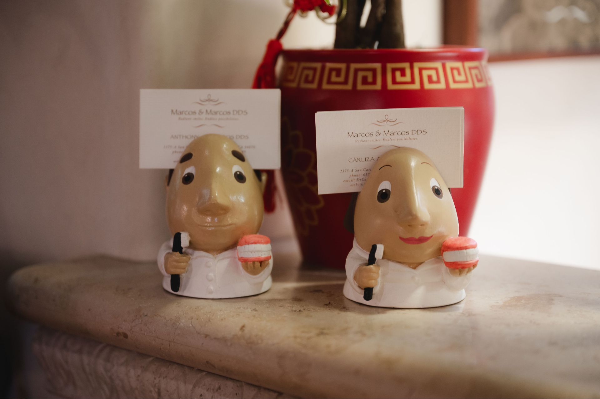 Two figurines holding toothbrushes and dentures, each supporting business cards.