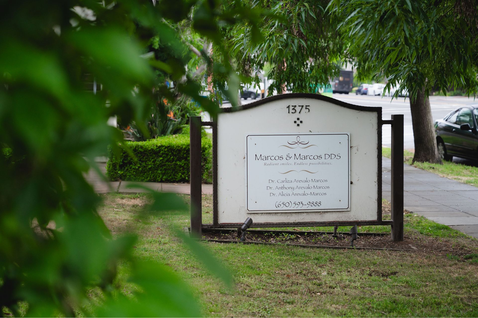 Outdoor sign for Marcos & Marcos DDS dental office with doctors' names and phone number.